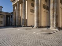 a street corner with several pillars and people walking in front of it and cars parked by