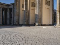 a street corner with several pillars and people walking in front of it and cars parked by