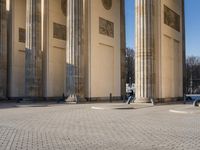 a street corner with several pillars and people walking in front of it and cars parked by