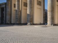 a street corner with several pillars and people walking in front of it and cars parked by