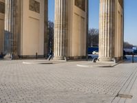 a street corner with several pillars and people walking in front of it and cars parked by
