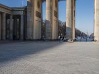a street corner with several pillars and people walking in front of it and cars parked by