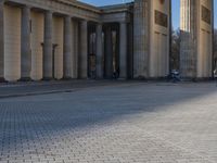a street corner with several pillars and people walking in front of it and cars parked by