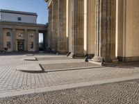 a street corner with several pillars and people walking in front of it and cars parked by