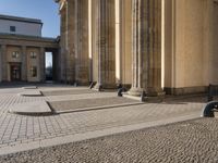 a street corner with several pillars and people walking in front of it and cars parked by