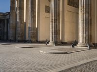 a street corner with several pillars and people walking in front of it and cars parked by