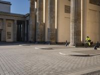 a street corner with several pillars and people walking in front of it and cars parked by