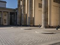 a street corner with several pillars and people walking in front of it and cars parked by