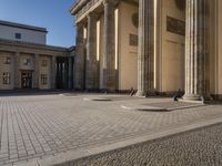 a street corner with several pillars and people walking in front of it and cars parked by