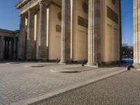 a street corner with several pillars and people walking in front of it and cars parked by