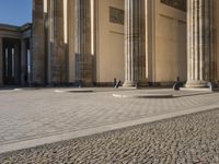 a street corner with several pillars and people walking in front of it and cars parked by