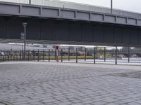 a man is skateboarding on a brick walkway by water near buildings and bridge overpass