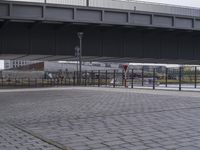 a man is skateboarding on a brick walkway by water near buildings and bridge overpass