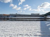 a snow covered yard with a bench and bridge in the background that has water on it