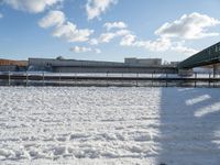 a snow covered yard with a bench and bridge in the background that has water on it