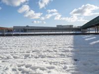 a snow covered yard with a bench and bridge in the background that has water on it