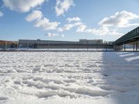 a snow covered yard with a bench and bridge in the background that has water on it