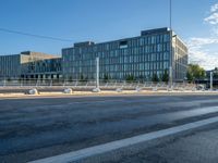 an empty road in front of a city building with many windows and some poles on either side