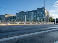 an empty road in front of a city building with many windows and some poles on either side