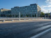 an empty road in front of a city building with many windows and some poles on either side