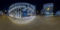 a fish - eye lens picture of a circular building at night with a person walking in front of it