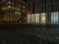 a square area with a table, chairs and benches at night time with lights from windows on the side