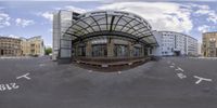 a fisheye view of an old building in the background is an empty street, with many buildings and a bus stop