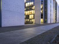 a tall building with some glass windows next to a sidewalk with people walking by it