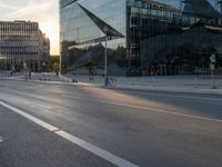 an empty city street next to glass and steel buildings with two bikes parked beside the road