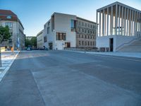 empty street lined with cement buildings next to a tall building with a staircase up to it