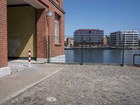 a red and white street pole is on the brick side of a building next to water