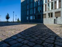 an empty brick street and the shadow of a building is cast on it by the sun