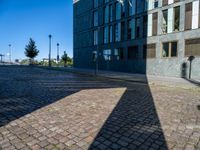 an empty brick street and the shadow of a building is cast on it by the sun