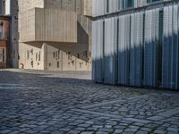 cobblestone driveway surrounded by modern buildings on sunny day with sun reflecting onto the windows