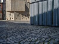 cobblestone driveway surrounded by modern buildings on sunny day with sun reflecting onto the windows