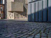 cobblestone driveway surrounded by modern buildings on sunny day with sun reflecting onto the windows