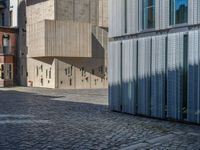 cobblestone driveway surrounded by modern buildings on sunny day with sun reflecting onto the windows