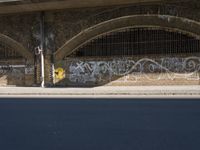 graffiti covered brick wall and gate under an overpass in an urban area with sun light