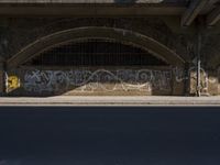 graffiti covered brick wall and gate under an overpass in an urban area with sun light