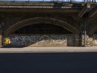 graffiti covered brick wall and gate under an overpass in an urban area with sun light