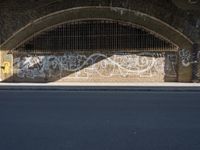 graffiti covered brick wall and gate under an overpass in an urban area with sun light
