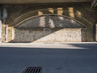 graffiti covered brick wall and gate under an overpass in an urban area with sun light