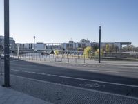 two lanes going through a city with some buildings behind it and a paved street with parking lot and fenced area