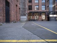 a view down an empty parking lot with two bicycles parked in the street below a large brick building