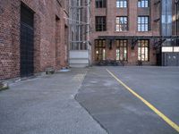 a view down an empty parking lot with two bicycles parked in the street below a large brick building