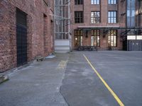 a view down an empty parking lot with two bicycles parked in the street below a large brick building