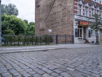 a street view with brick road in front of a restaurant and fence in the foreground