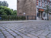 a street view with brick road in front of a restaurant and fence in the foreground