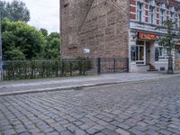 a street view with brick road in front of a restaurant and fence in the foreground