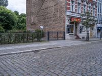 a street view with brick road in front of a restaurant and fence in the foreground